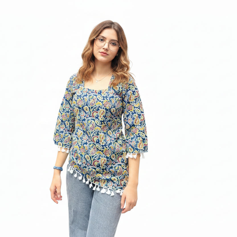 Woman wearing an indigo blue paisley print short kurti with an asymmetric high-low hem and white tassel lace trim, paired with gray jeans.