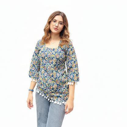 Woman wearing an indigo blue paisley print short kurti with an asymmetric high-low hem and white tassel lace trim, paired with gray jeans.