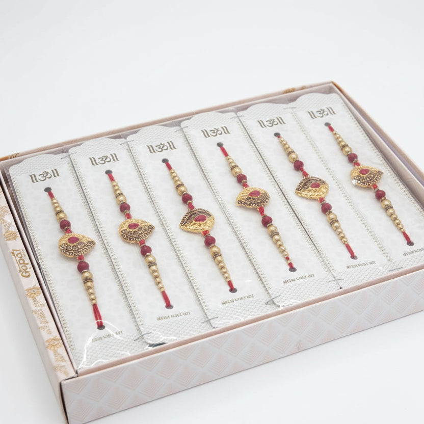 Elegant gold beaded rakhi set with red thread and ornamental design